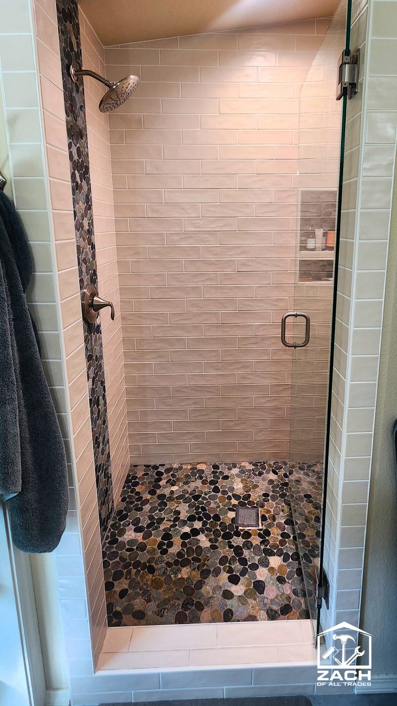 Cream subway tile shower with vertical pebble accent strip and pebble floor