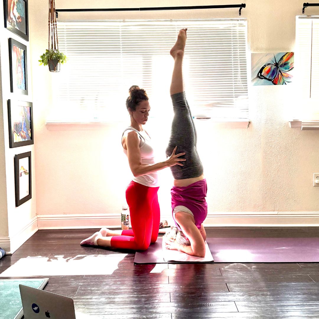 Krista guiding a student through a supported headstand