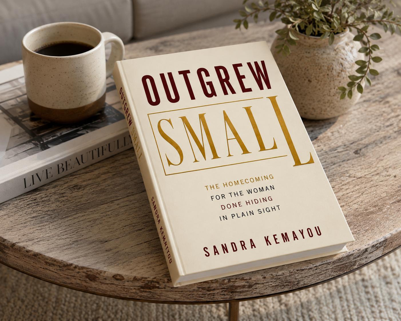Outgrew Small by Sandra Kemayou — book on a wooden coffee table with a ceramic mug and a small potted plant