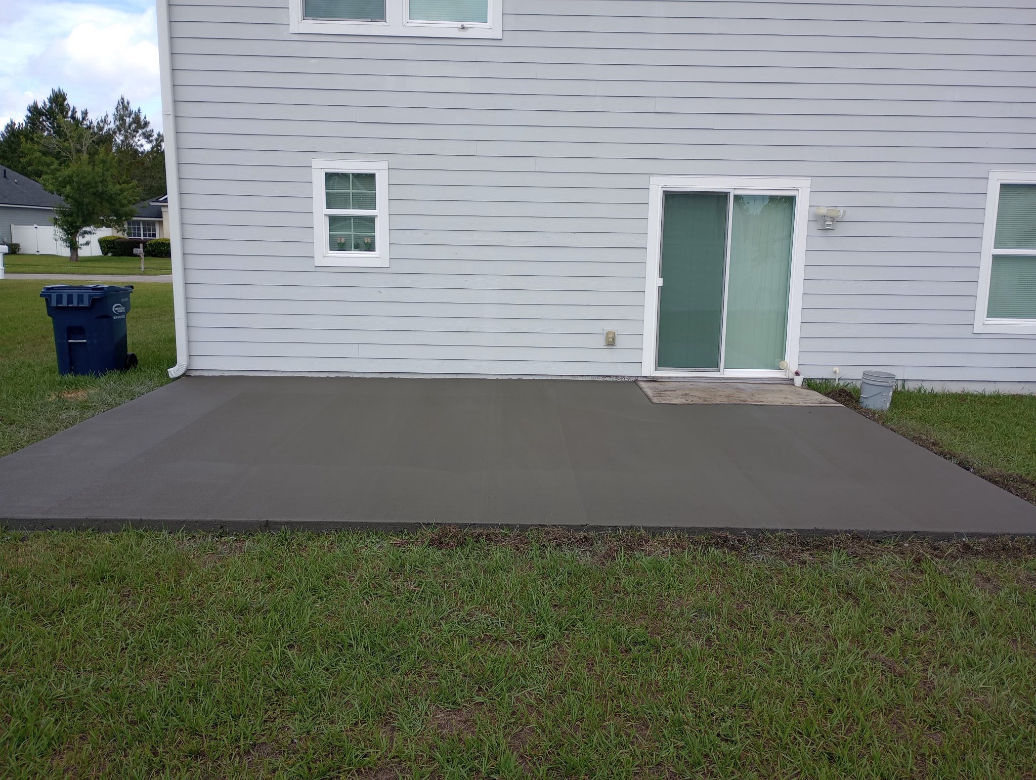 A freshly poured backyard patio slab on a suburban home, with the surrounding lawn left clean and untouched