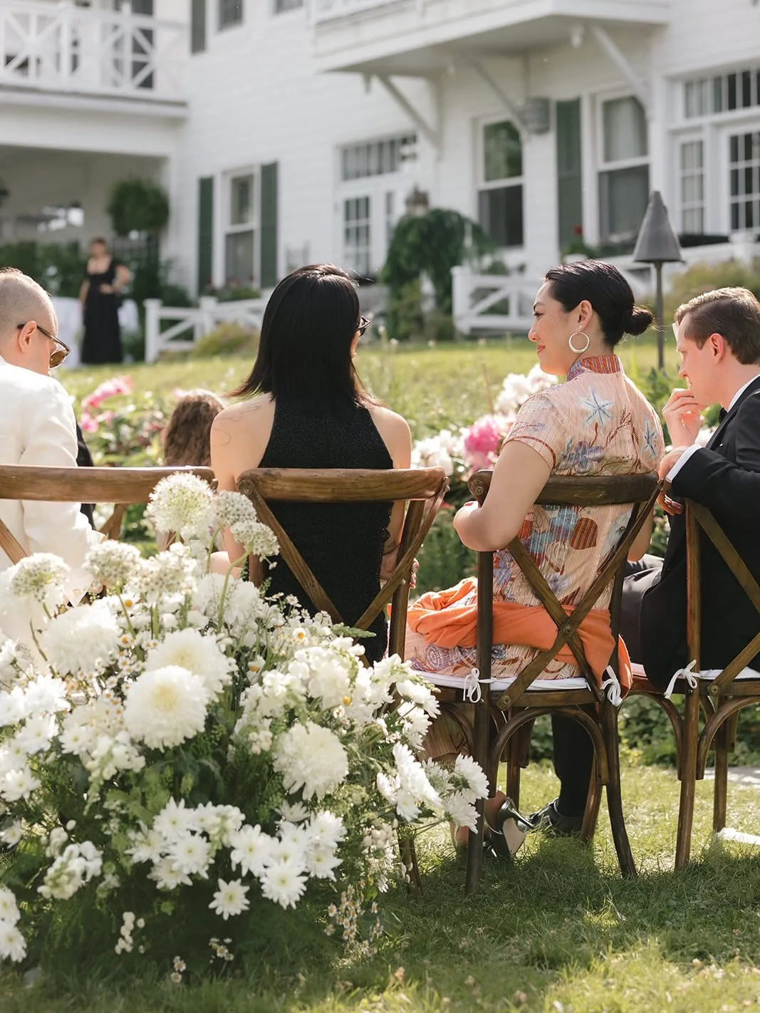 Fresh white flowers and greenery beside wooden chairs at an outdoor wedding