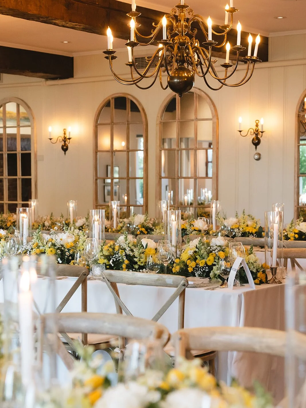 Fresh yellow and white wedding centrepieces with greenery and glass candle holders