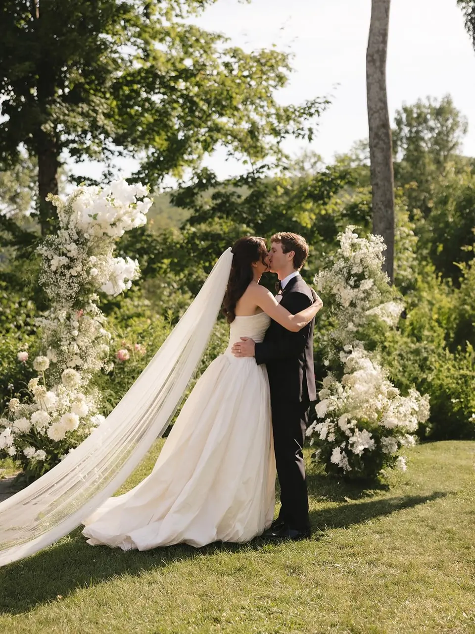 Couple beside fresh white floral arrangements at an outdoor wedding ceremony