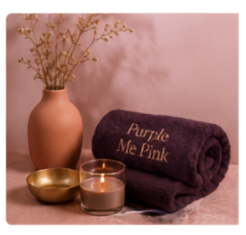 A rolled Purple Me Pink towel beside a candle and a vase