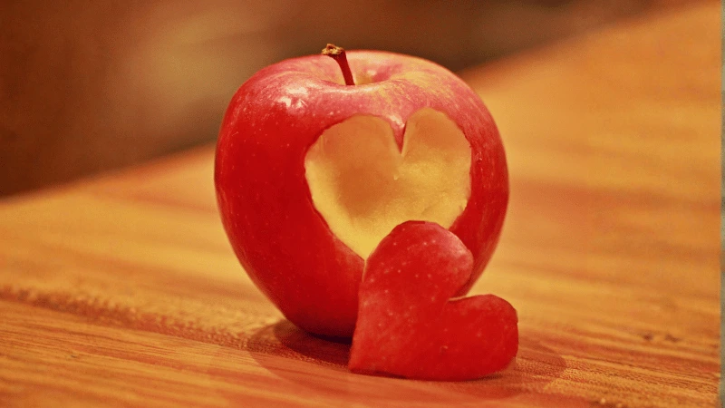 A red apple with a heart-shaped piece carved out, resting on a warm wooden surface - a symbol of self-compassion and nurturing our inner world