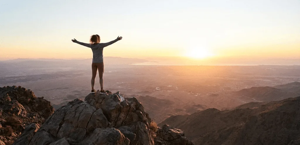 Person with arms raised on a mountaintop at sunrise