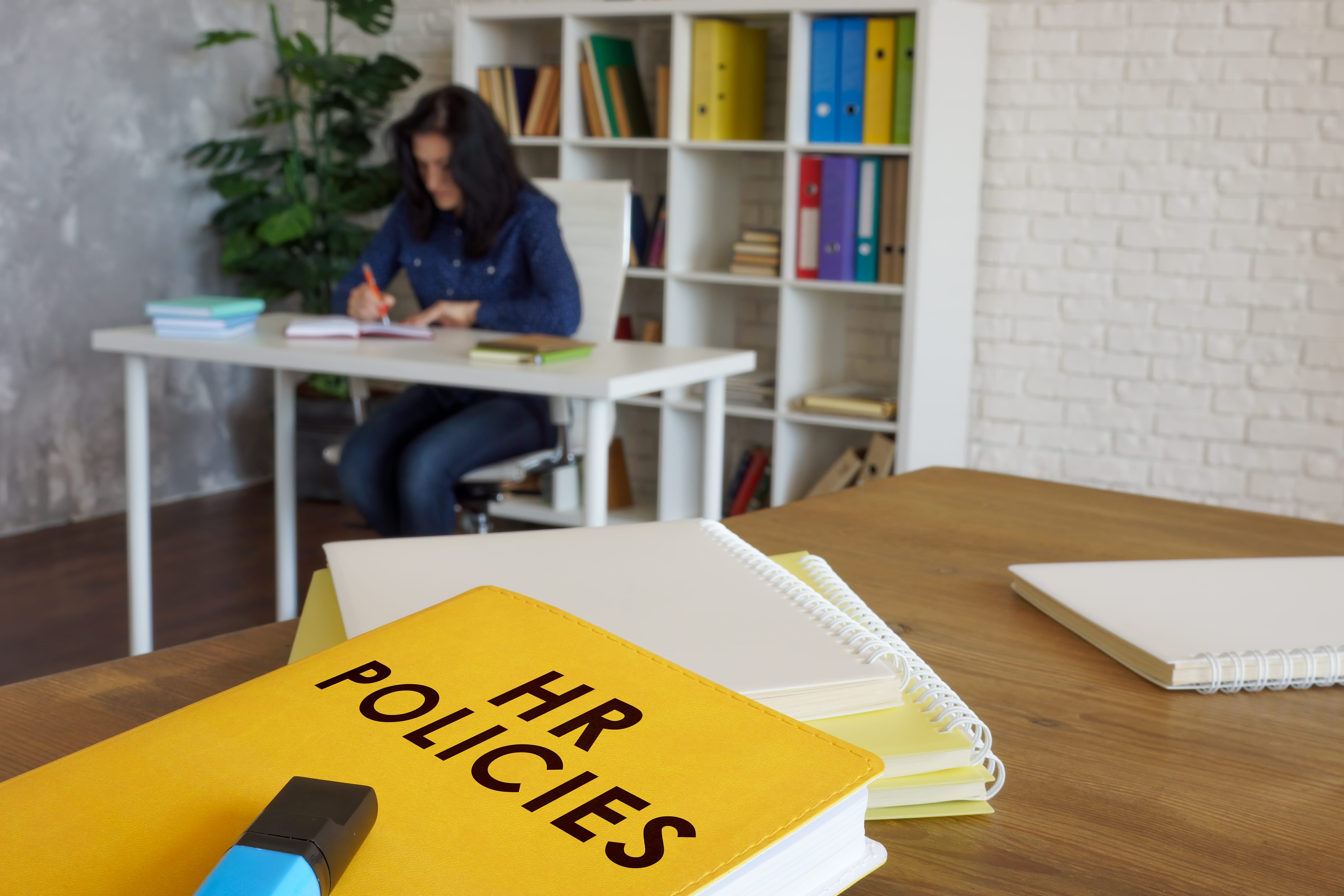 Lady working in the background with the HR policy book in focus Lady working in the background with the HR policy book in focus