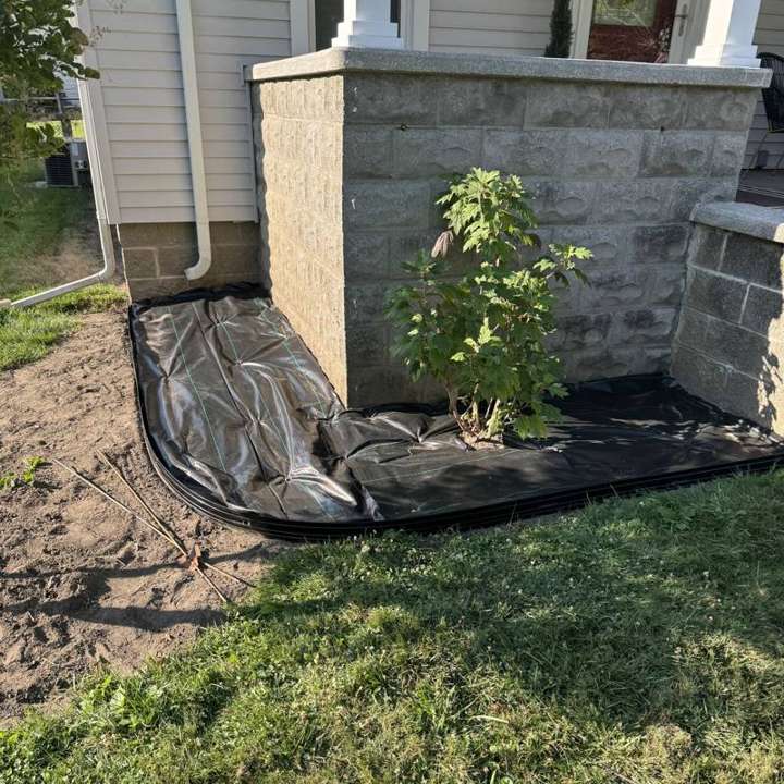 Landscape fabric and edging being installed beside a porch