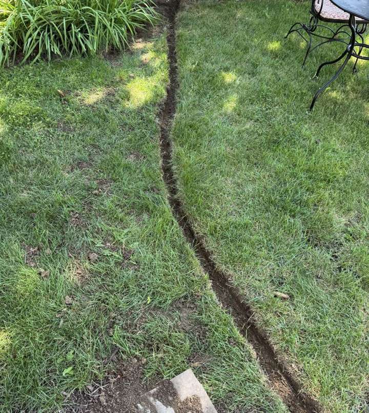 A drainage trench being cut across a backyard lawn