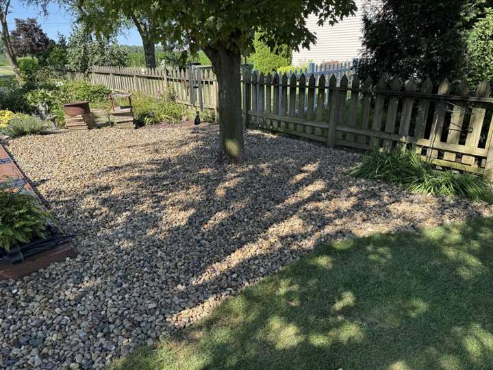 River rock bed under a shade tree along a wooden fence