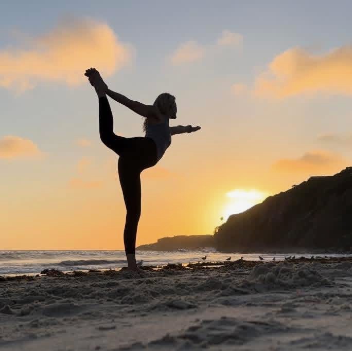 Dotty Sunshine in dancer pose on the beach at sunset representing vibrant health and wellness