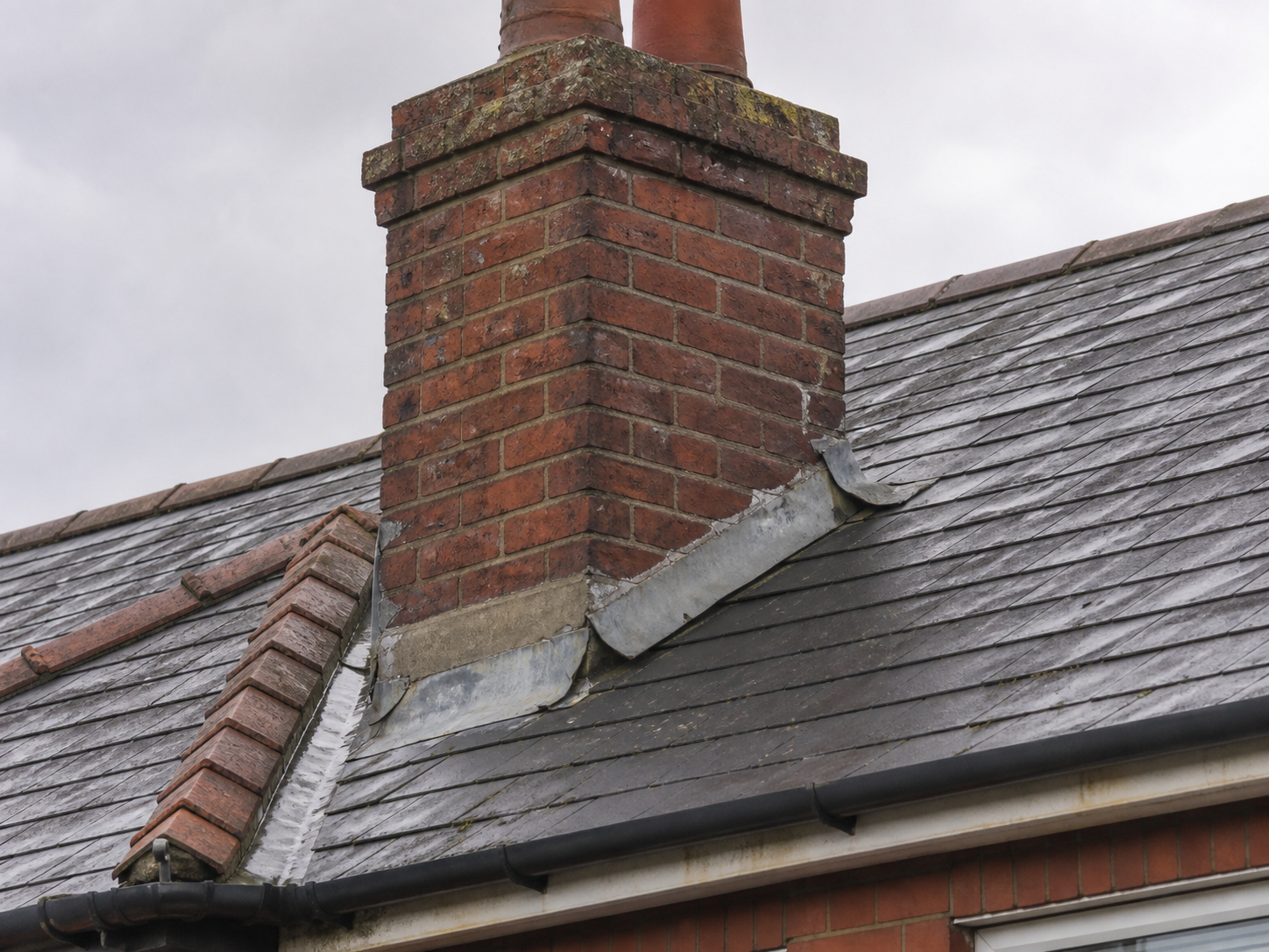 Weathered Northern Irish brick chimney with failed lead flashing at the roof junction