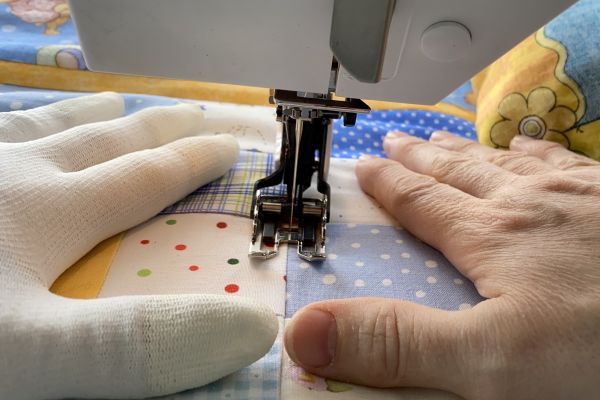 Hender som beveger en quilt under nåla på en symaskin