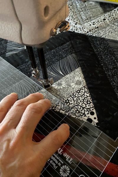 Quilt på longarm. Nærbilde av foten. En hånd holder en linjal inntil foten