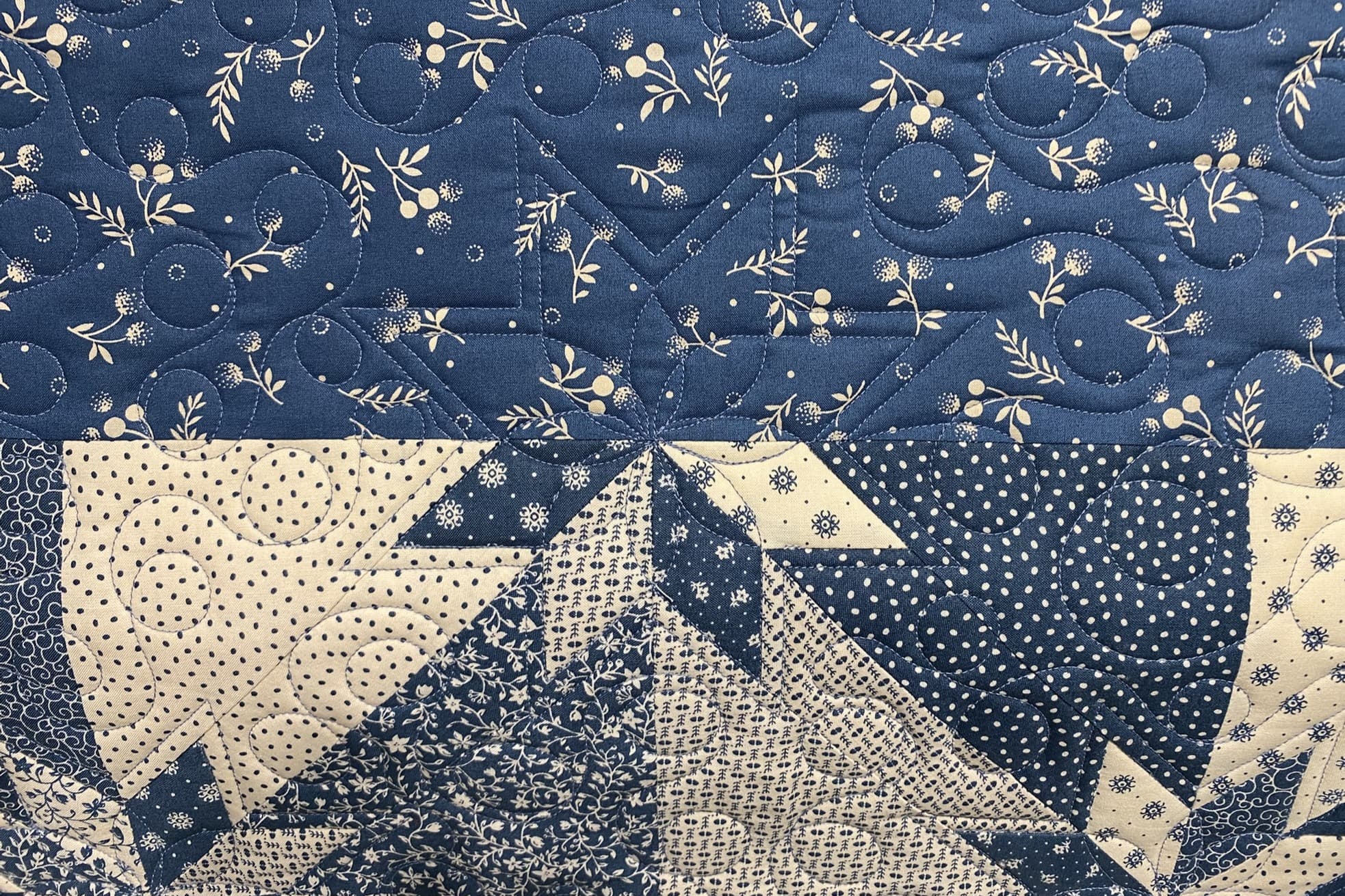 Utsnitt av blå og kremhvit quilt i mønsteret Hunter's star. Det er ekkoquiltet rundt stjernene og quiltet enkle loops i bakgrunnen