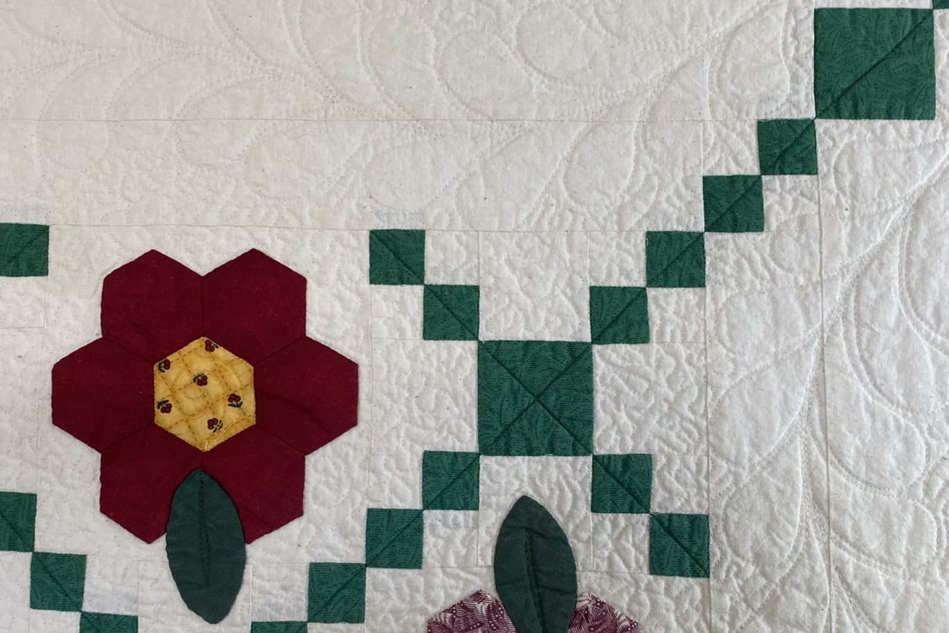 Utsnitt av en liten quilt, blomst av sekskanter på lys bakgrunn. Quiltet med en fjær og stippling i bakgrunnen