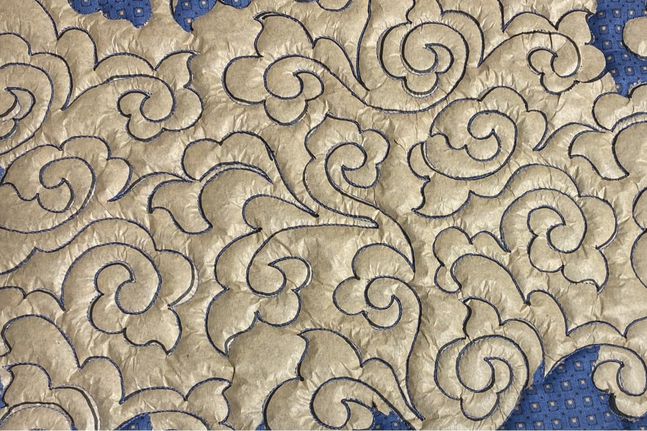 Nærbilde av quilting. Mønsteret er tegnet på papir, som deretter er lagt oppå stoffet og quiltet gjennom