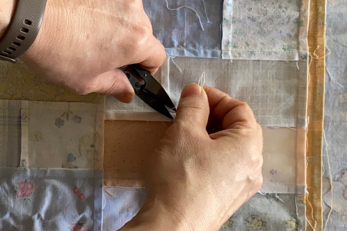 Nærbilde av hender med liten saks som fjerner tråder fra baksiden av en quilt