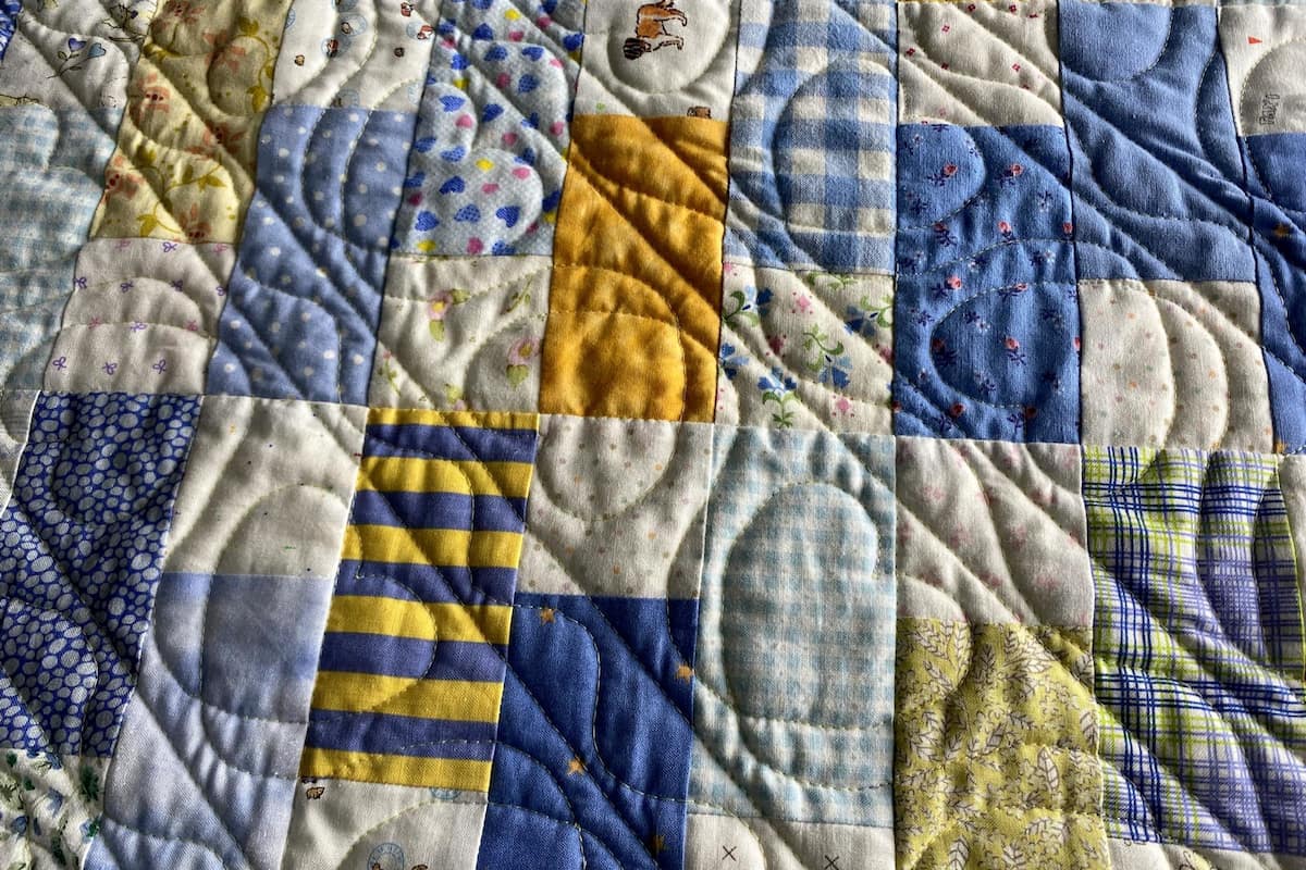 nærbilde av en blå, hvit og gul quilttopp. Det er quiltet diagonale linjer og hjerter.
