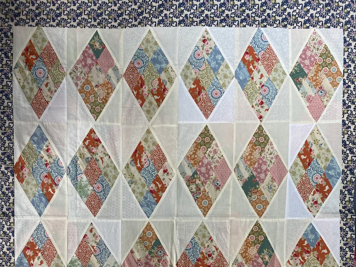 Bilde av en uquiltet topp i lyse og delikate farger. Lyse diamanter alternerer med mønstrede diamanter. Toppen har en smal bord i blåtoner.