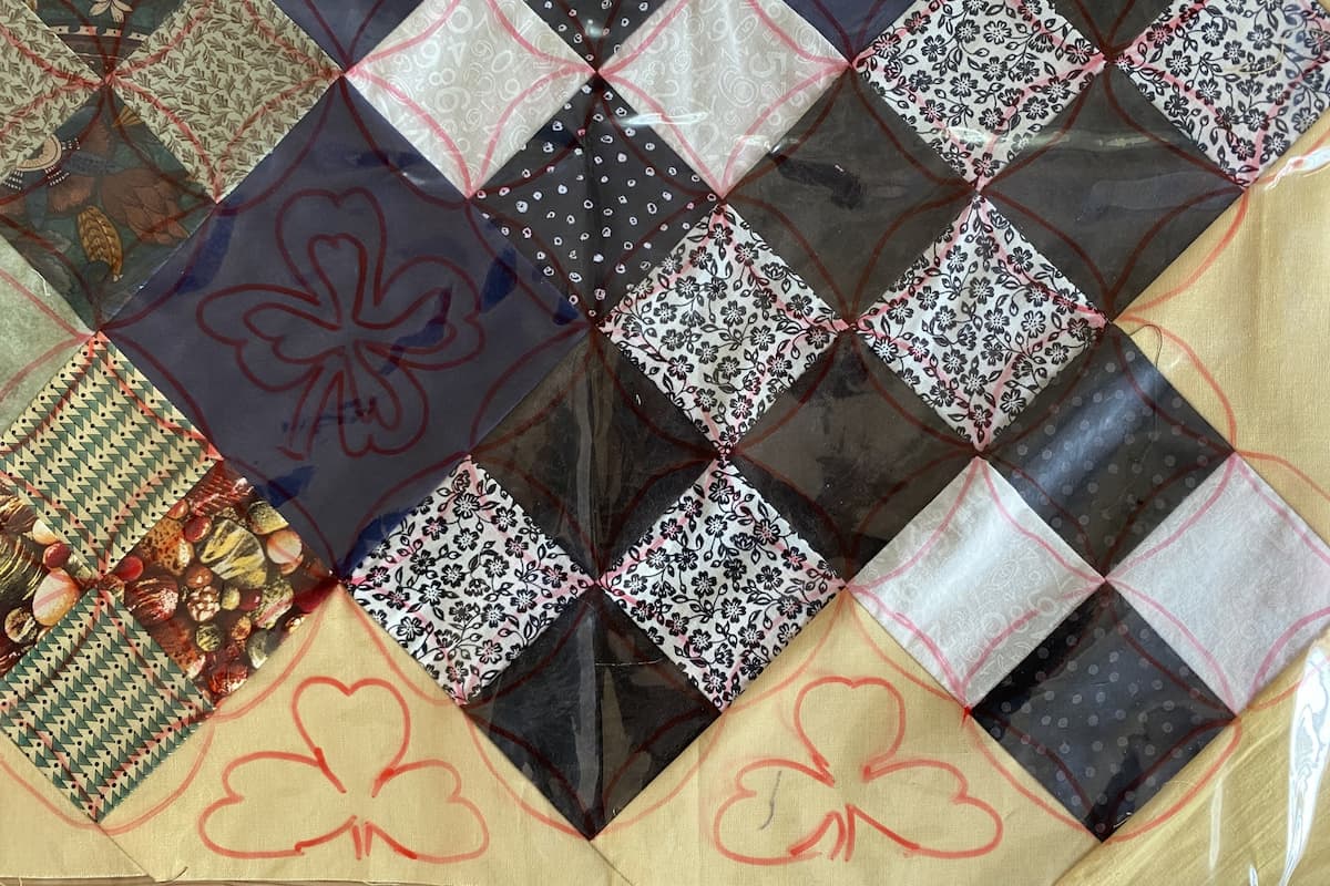 Utsnitt av en quilt dekket med gjennomsiktig plast og ulike forslag til quiltedesign tegnet på plasten.