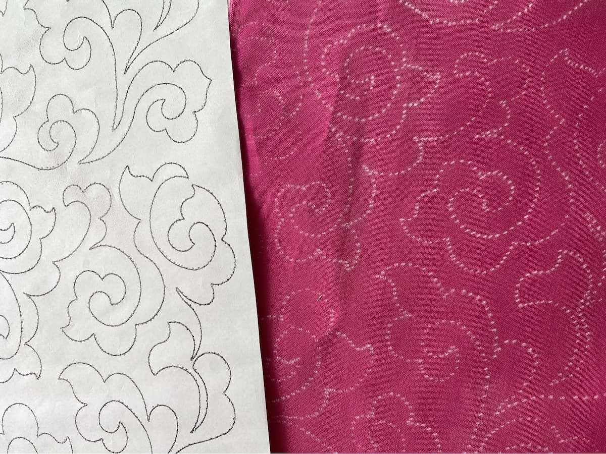 En papirstensil ligger delvis oppå et rosa stykke stoff markert med hvite krittmarkeringer fra stensilen En papirstensil ligger delvis oppå et rosa stykke stoff markert med hvite krittmarkeringer fra stensilen