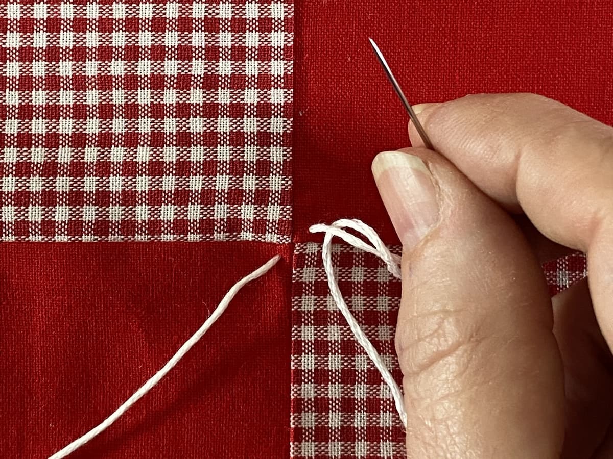 Nærbilde av en rød og hvit quilt med en hvit tråd for knyting 