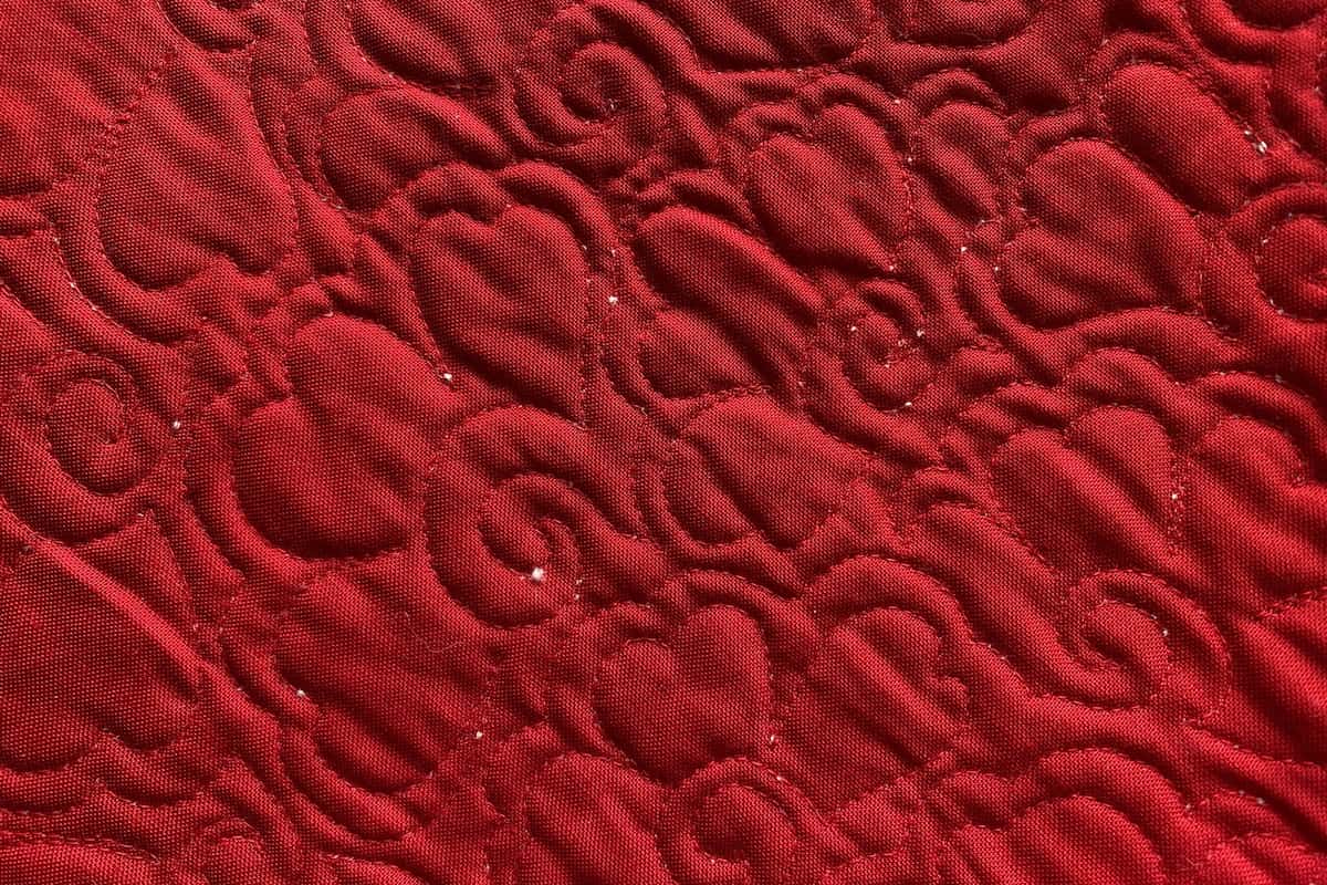 Den røde baksiden av en quilt. Quiltet med rødt tråd. du ser tydelig hvor små tuser av vatt er blitt med ut på baksiden under quiltingen