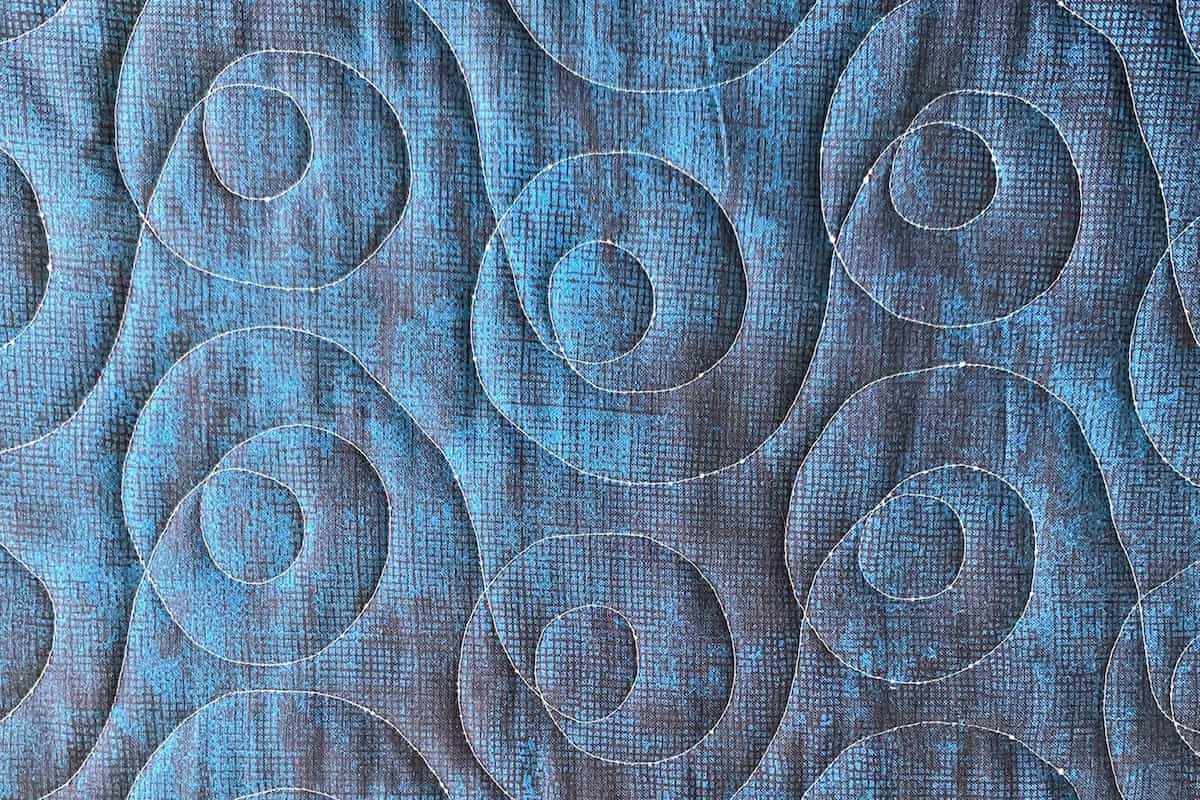 Baksiden av en quilt i blåtoner. Quiltingen i en lysere trådfarge er tydelig