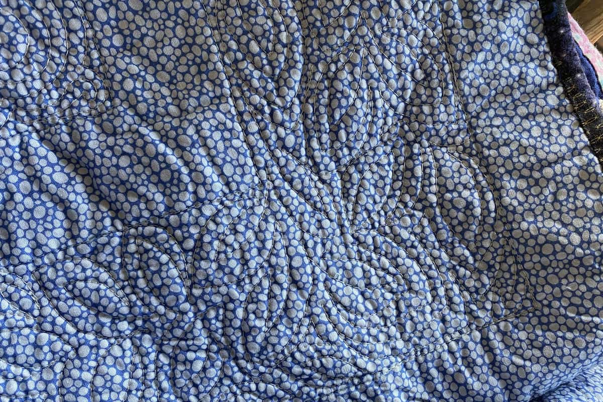 baksiden av en quilt med et mønstrete stoff. Quiltingen i en tråd som matcher quilten er lite synlig, du ser mest tekstur