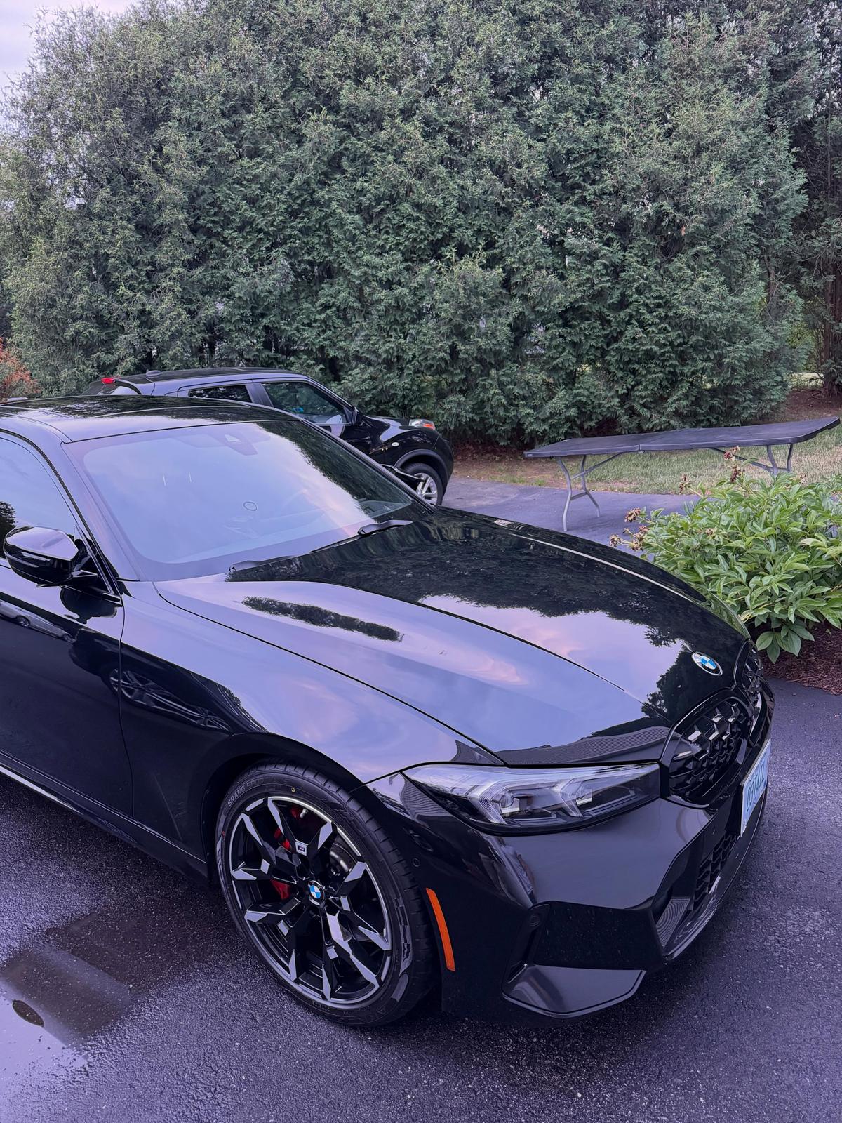 A gloss black 2025 BMW M340i with red brake calipers, freshly detailed and beaded with water