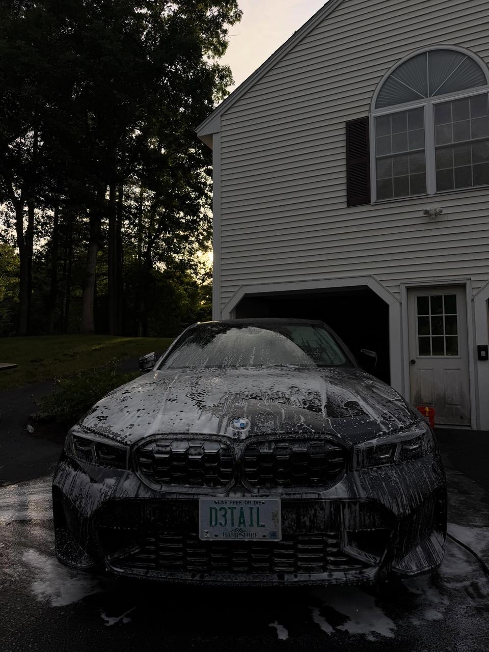 A black BMW covered in foam pre-wash at dusk
