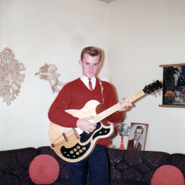 A young Buford Jones in a red sweater and tie holding an electric guitar