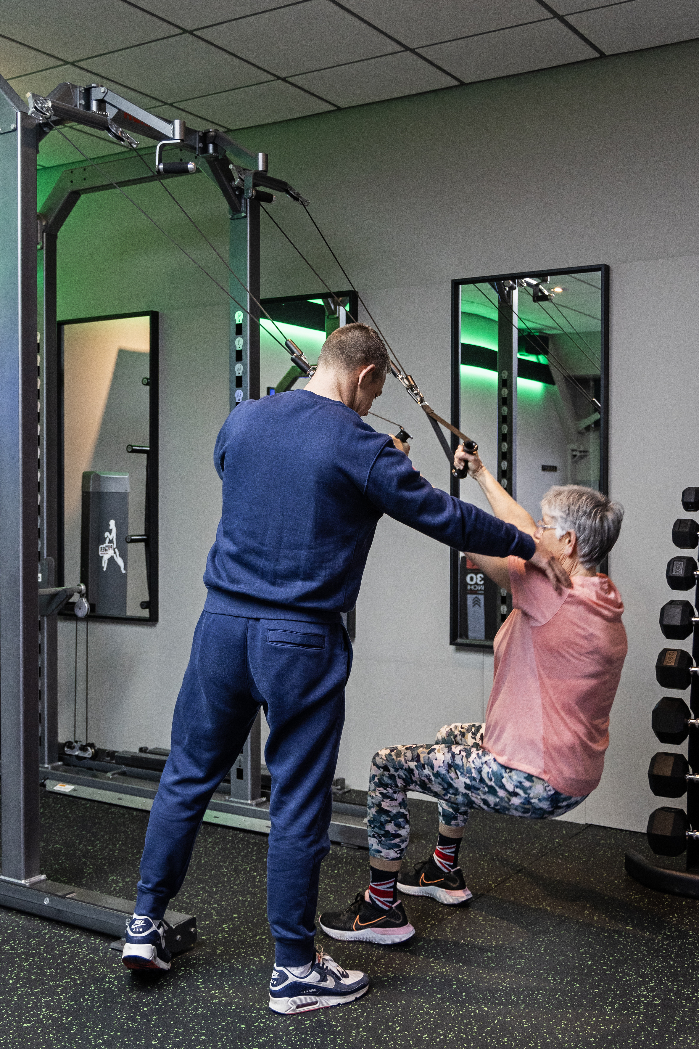 Een PTL-coach begeleidt een member bij een trainingstoestel