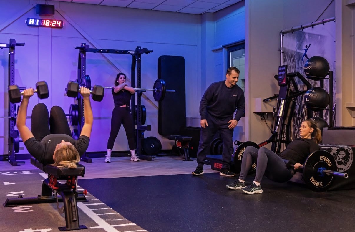 Een PTL-coach begeleidt drie members met verschillende oefeningen in een kleine groep