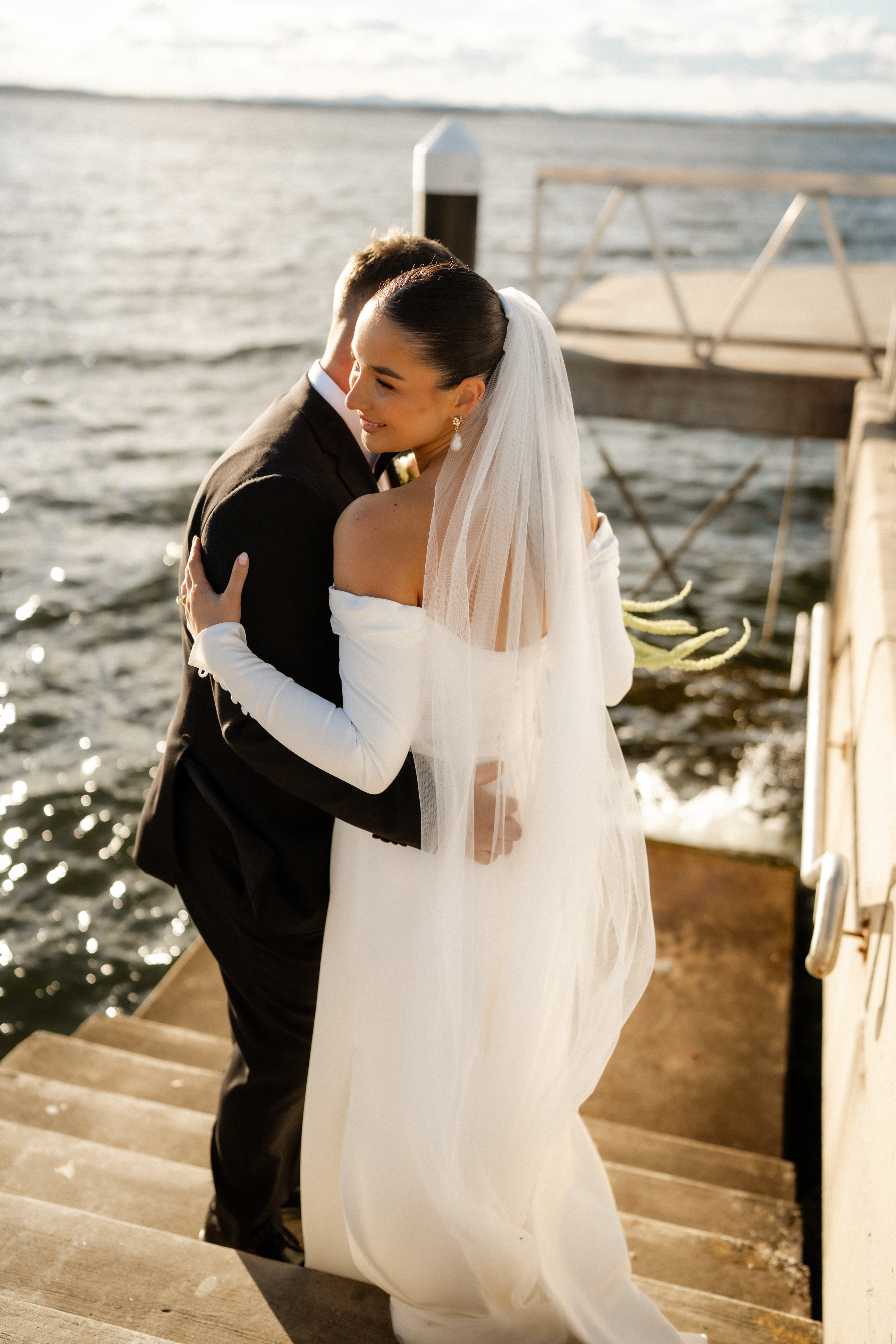 Couple on jetty stairs, veil lifting, water behind them