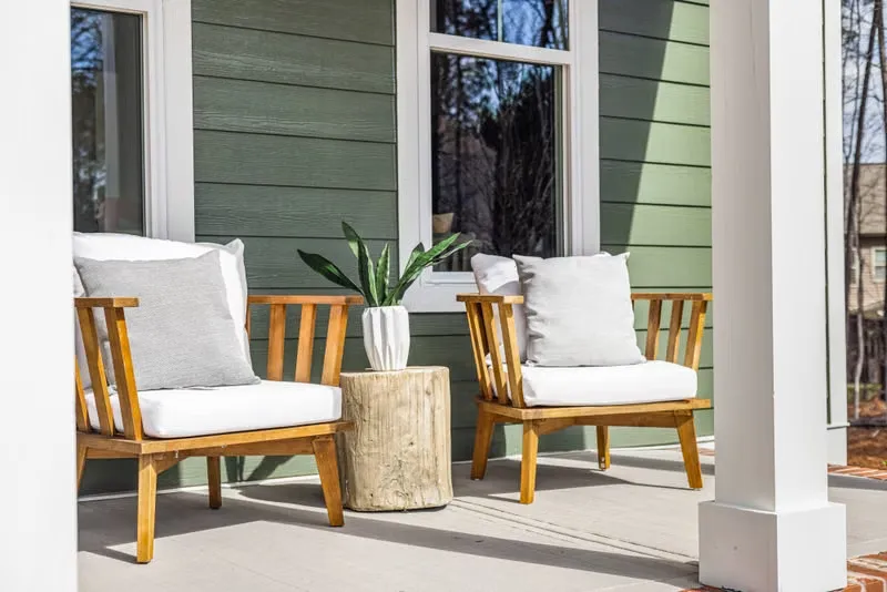 Covered front porch with green siding, a white porch column, and two wooden armchairs