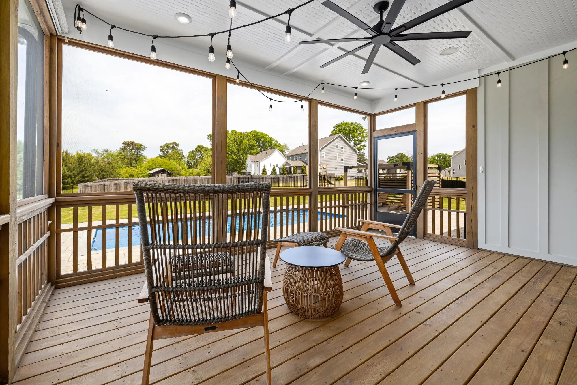 Screened porch with string lights and a ceiling fan overlooking a pool and landscaped backyard