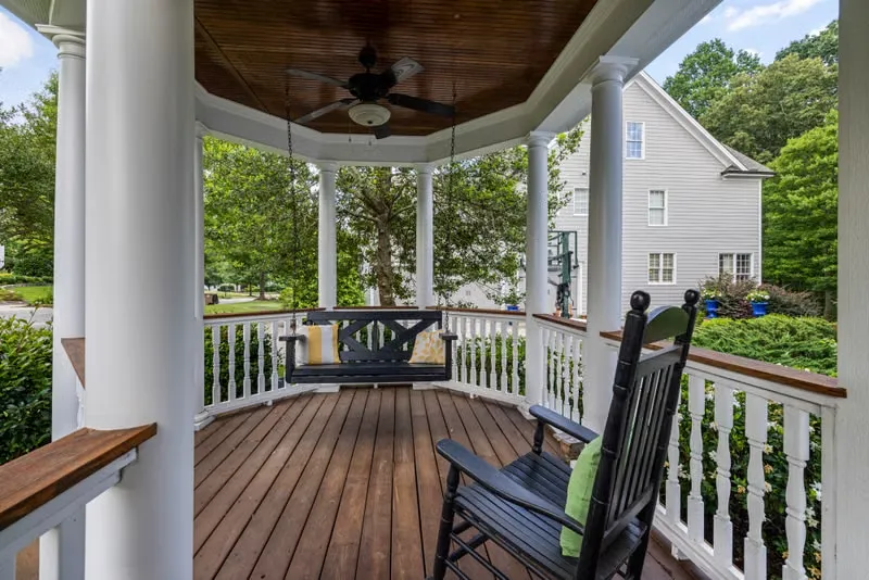 Round covered porch with a ceiling fan, a cushioned porch swing and a rocking chair