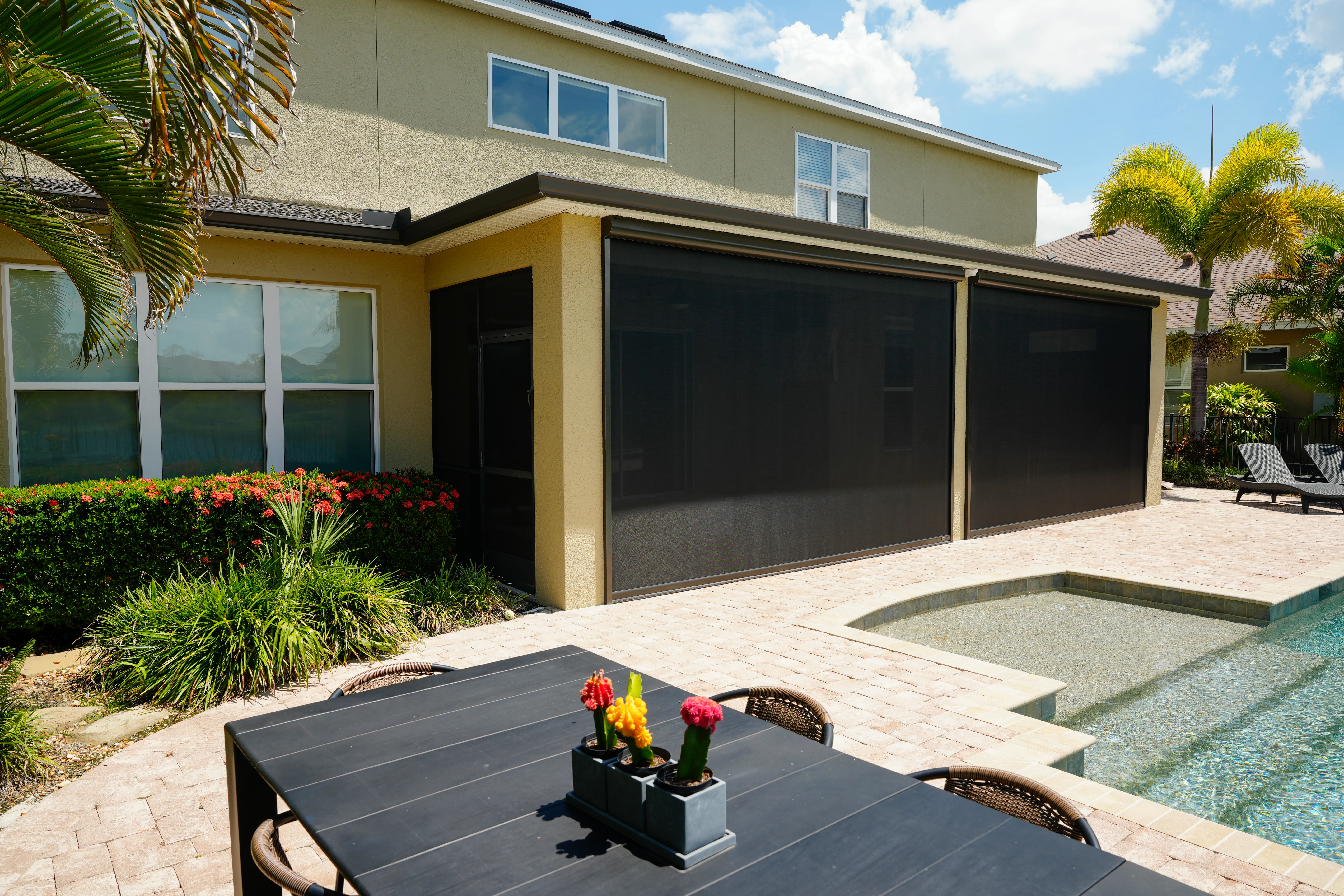 Retractable solar screens extended along a two-story stucco home beside a pool and spa