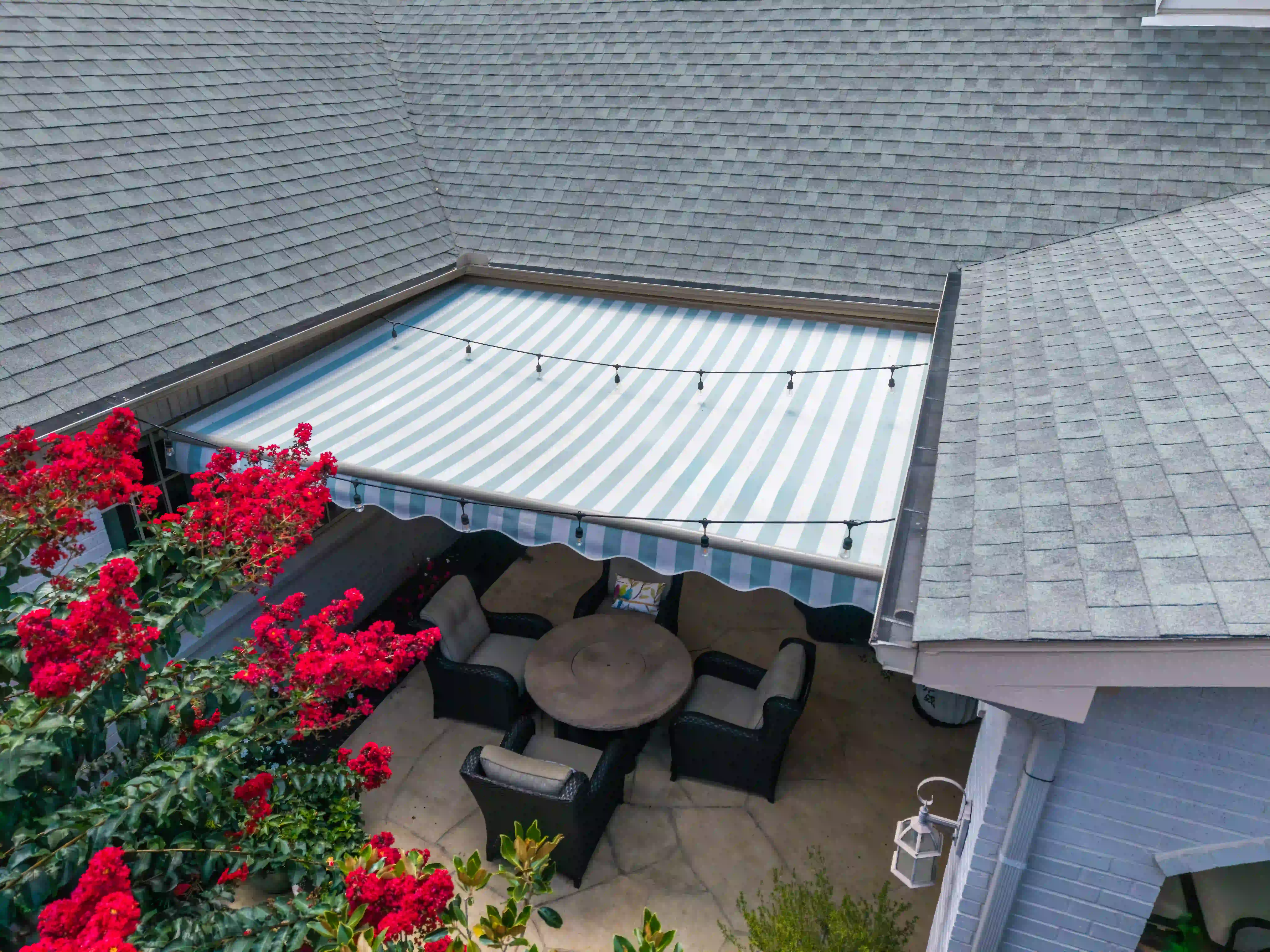 Striped retractable awning extended over a furnished patio dining set with string lights