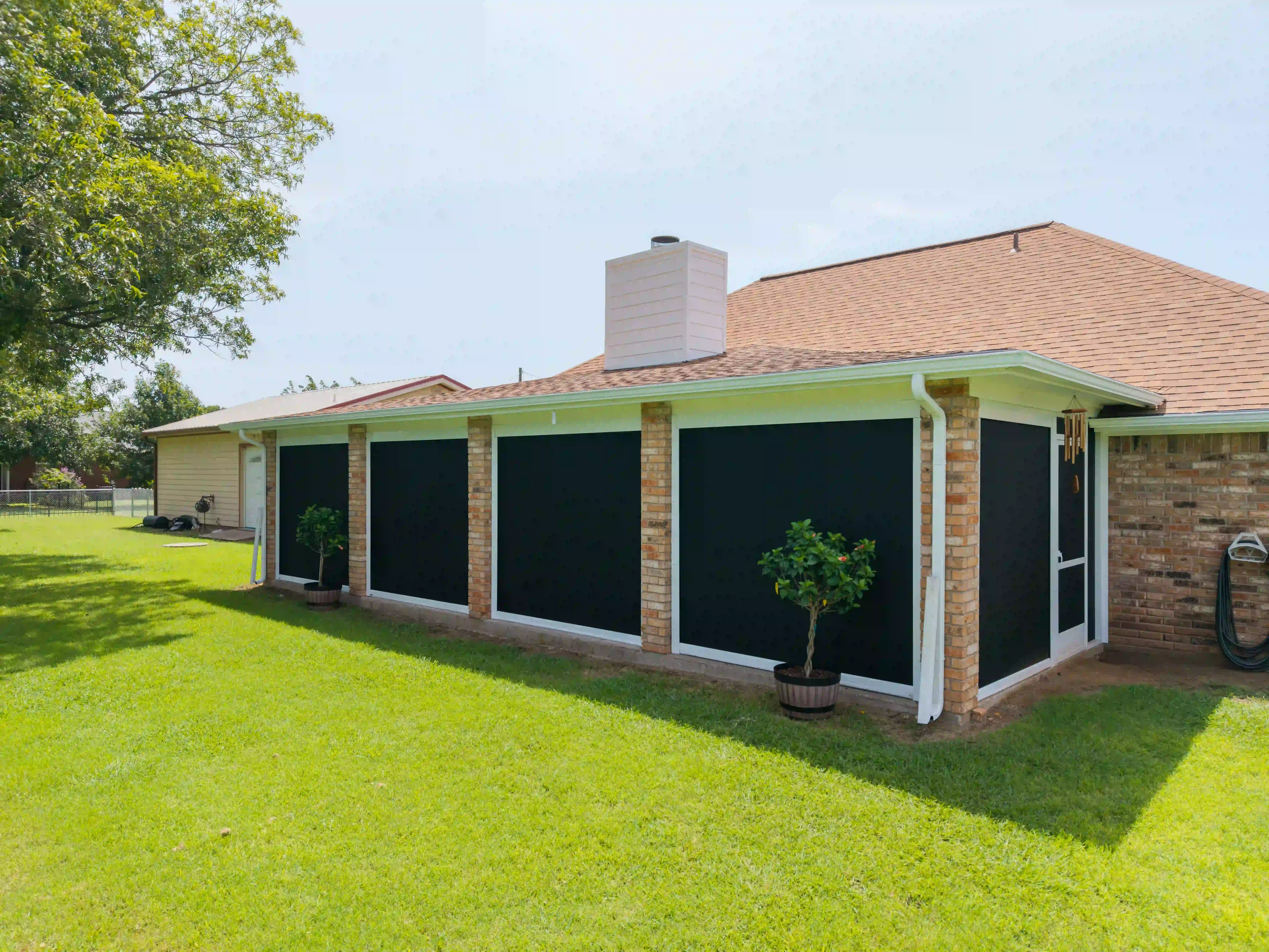 Red-brick house with four black solar screens fully extended along the patio