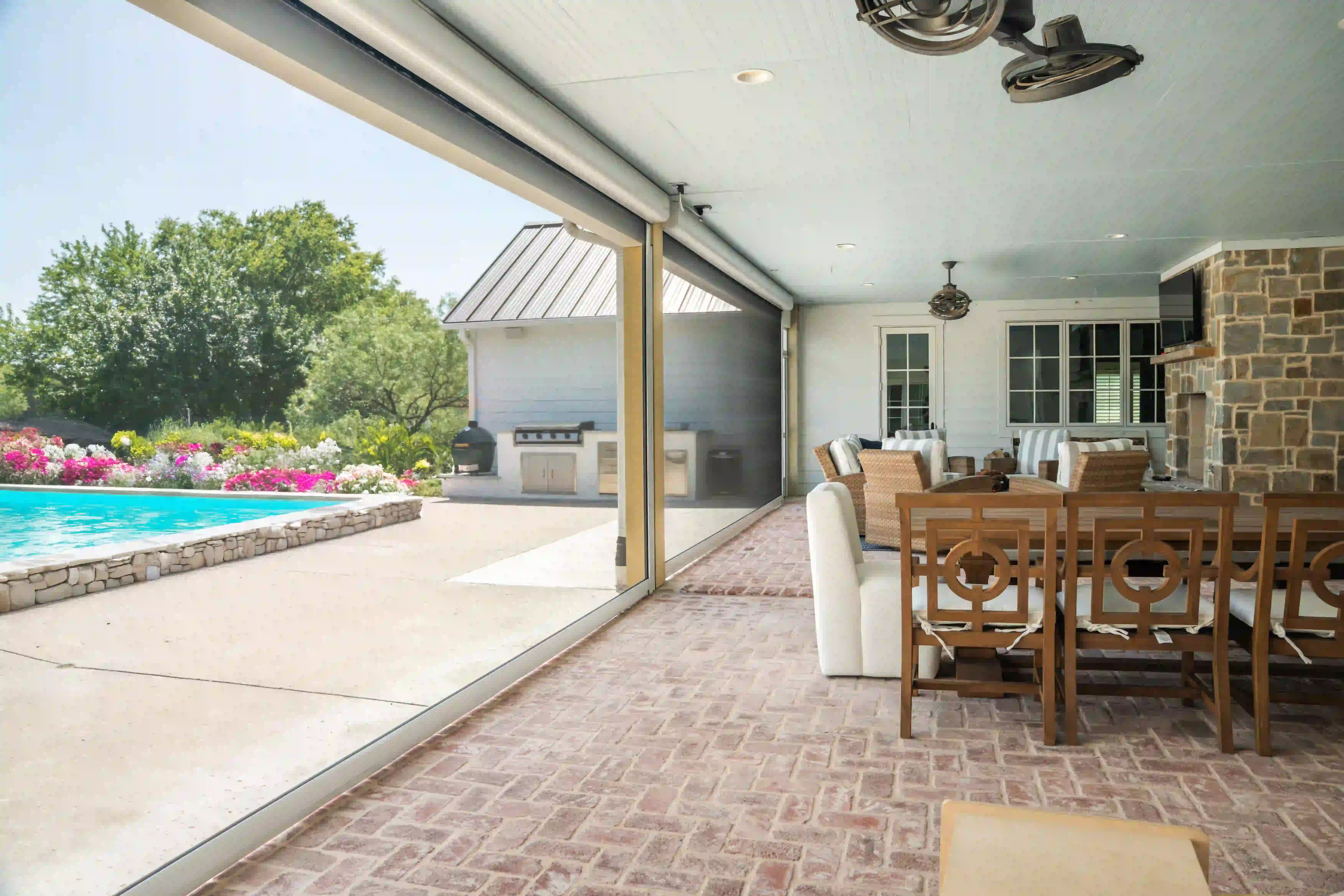 Covered patio with an outdoor kitchen, dining set and pool view through a retracting screen