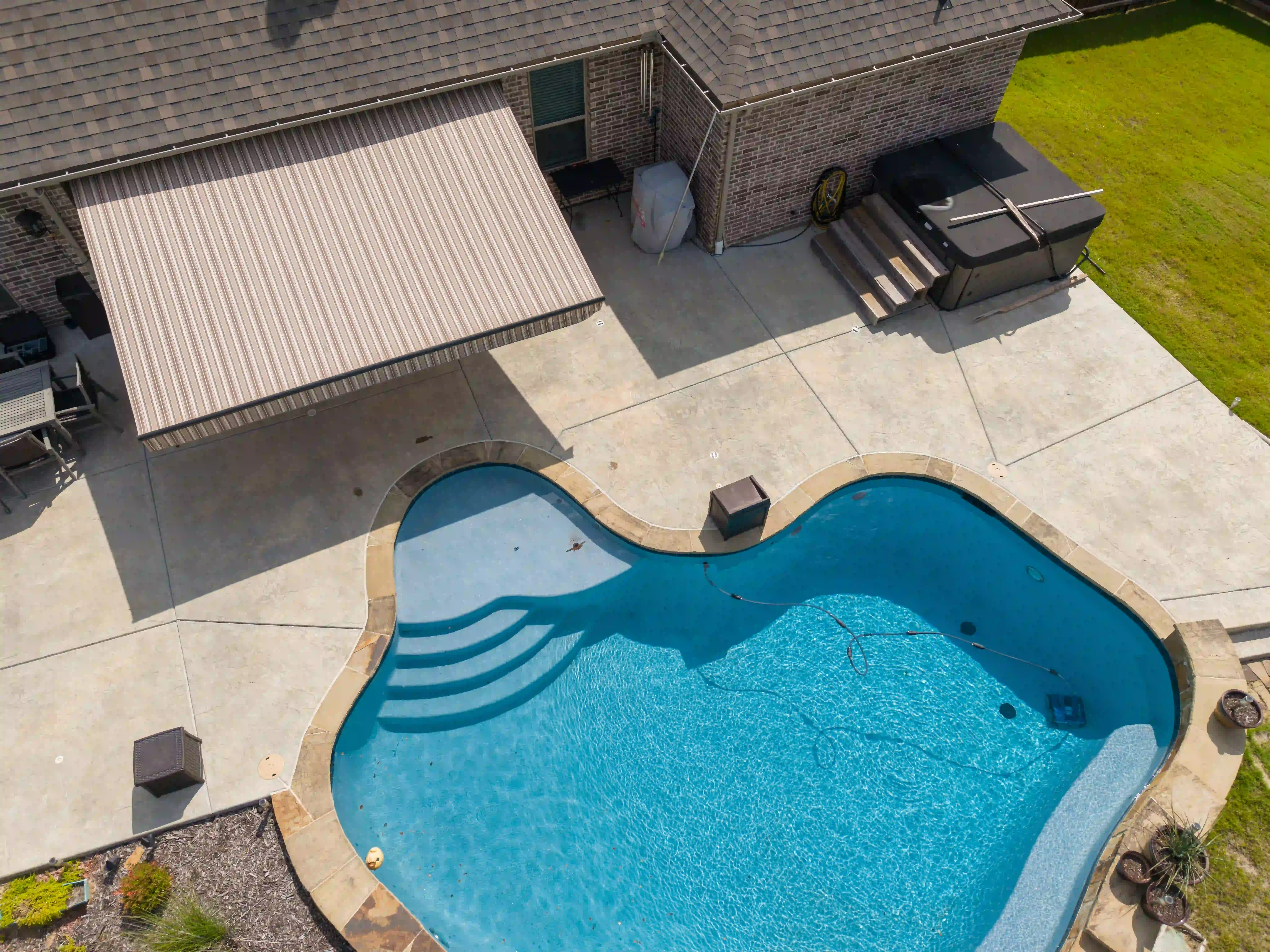 Aerial view of a brick house with a covered patio awning and backyard pool
