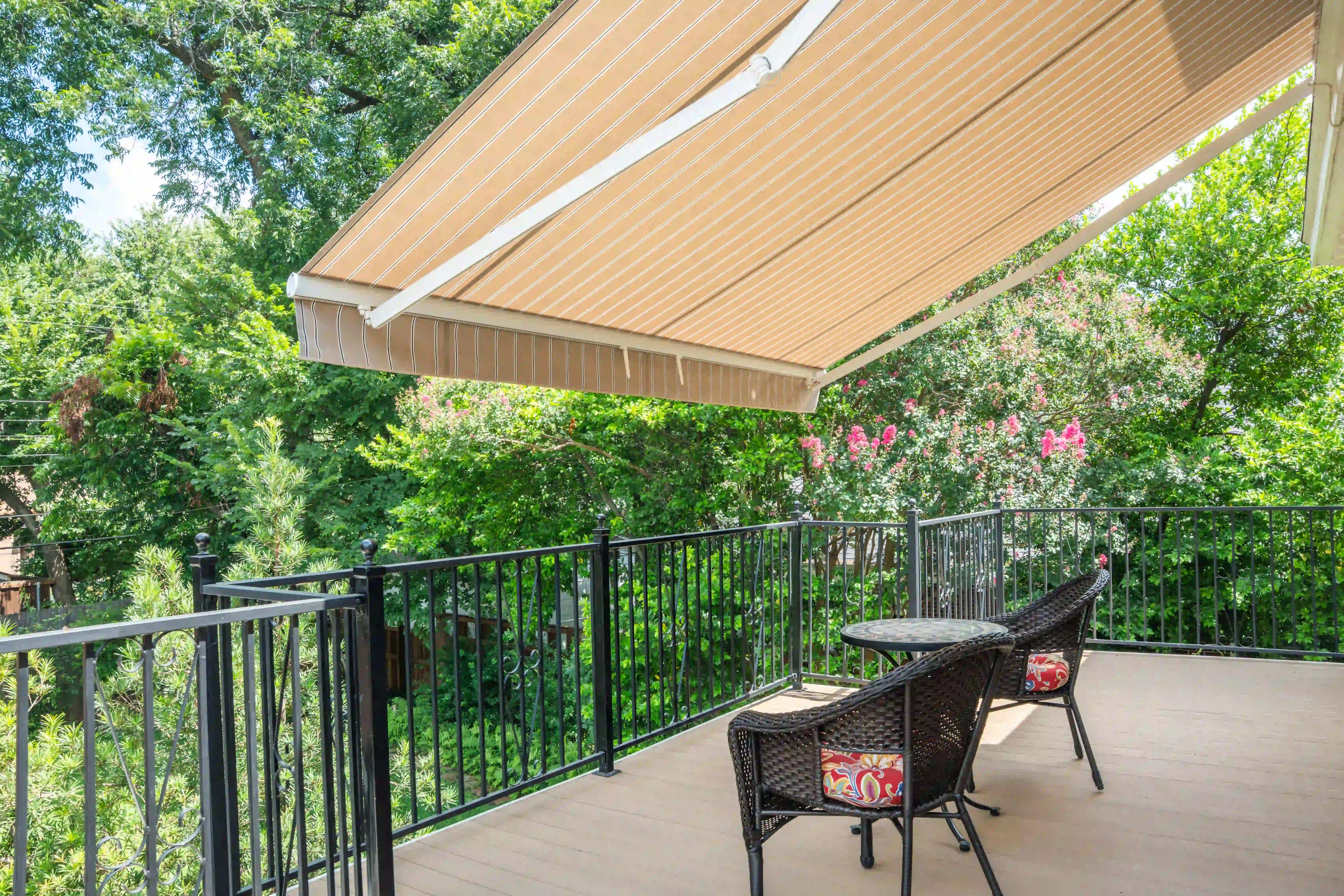 Striped awning shading a deck with wicker chairs under a shaded tree canopy