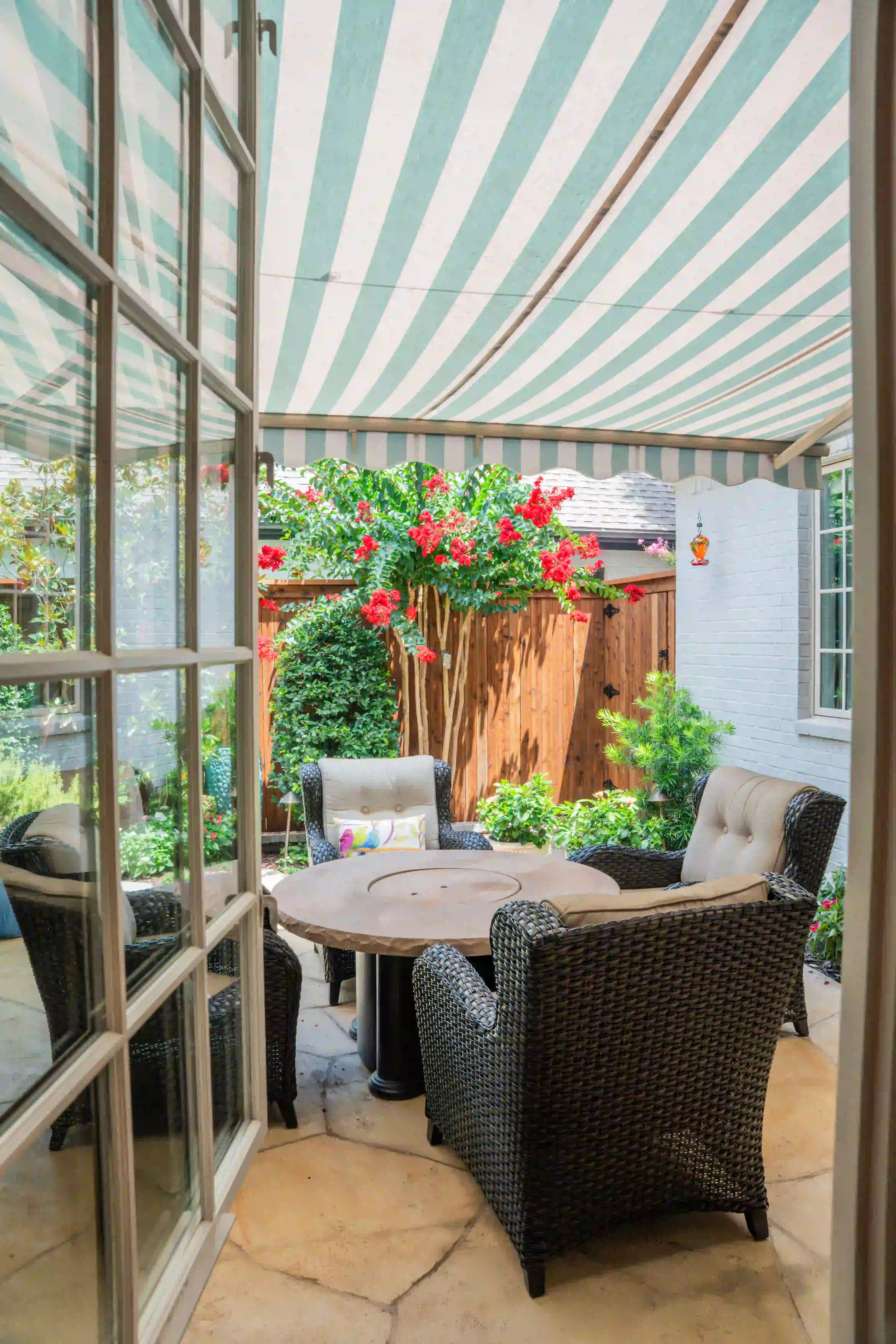 Courtyard patio with a striped awning, wicker chairs and blooming crepe myrtle against a white brick house