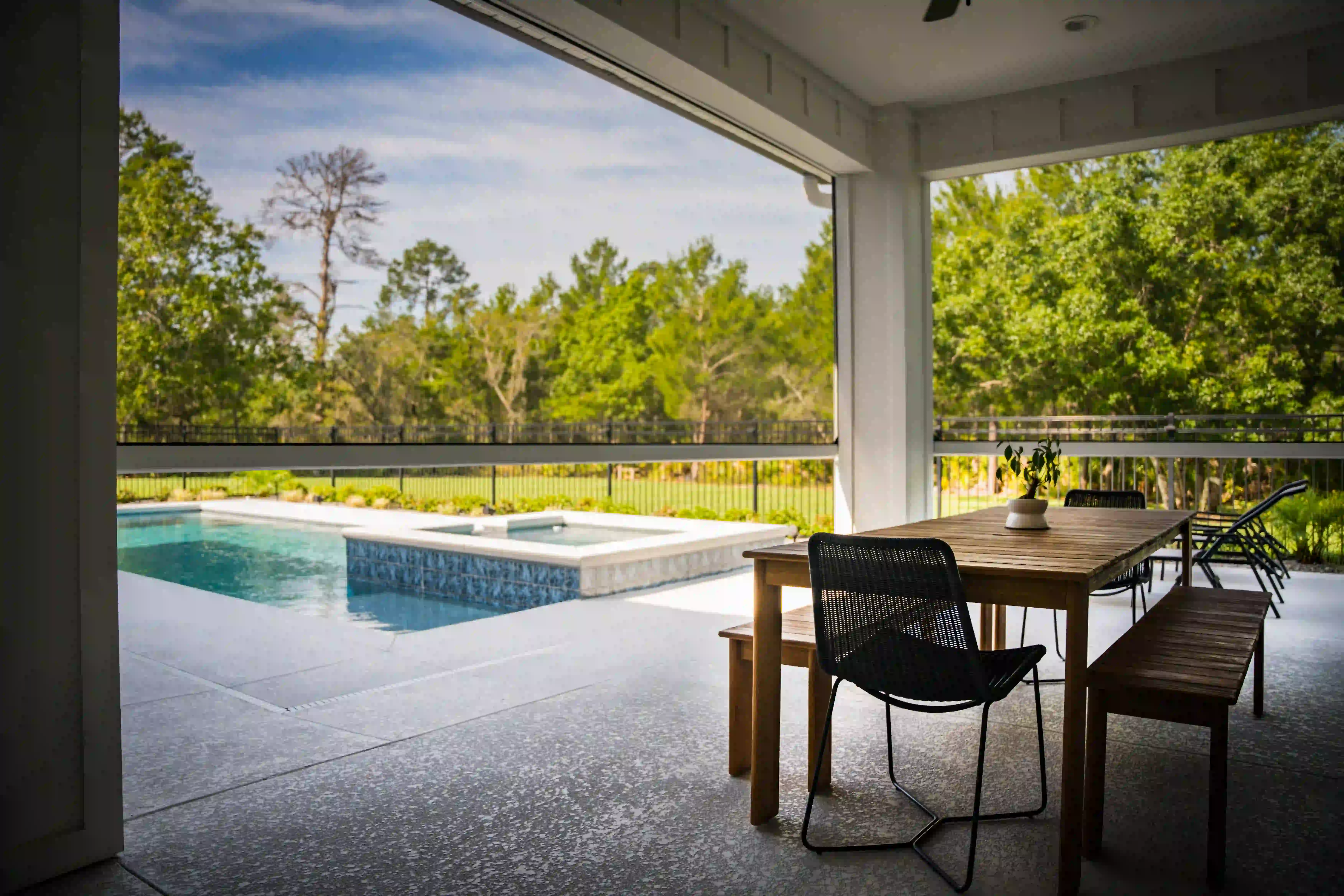 Screened dining porch looking out at dense pine and hardwood canopy through a black metal fence