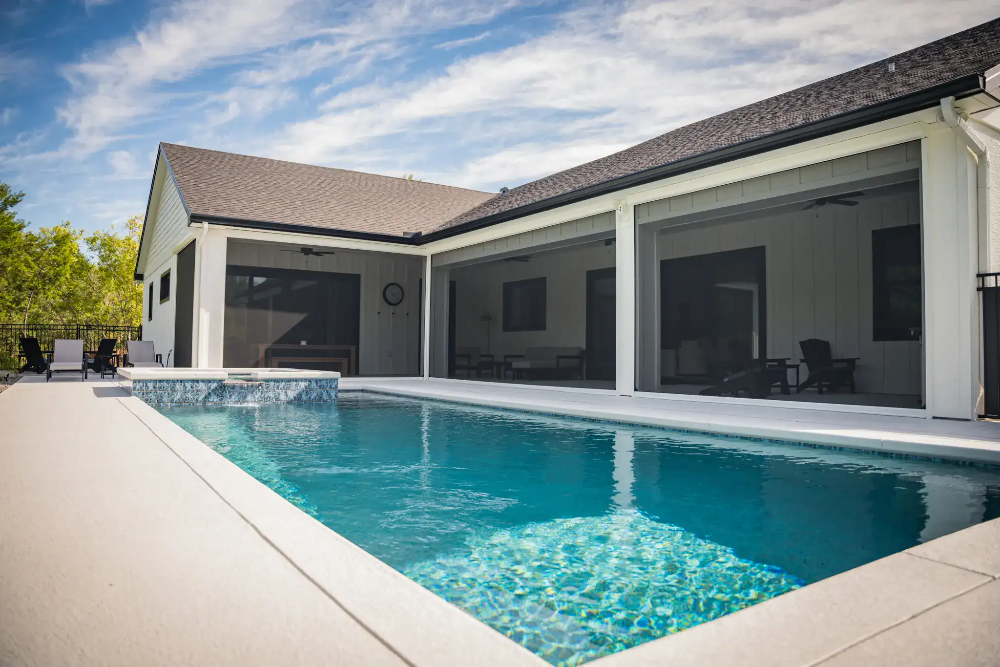Farmhouse-style home with a screened porch, pool and black metal fence under dense tree canopy