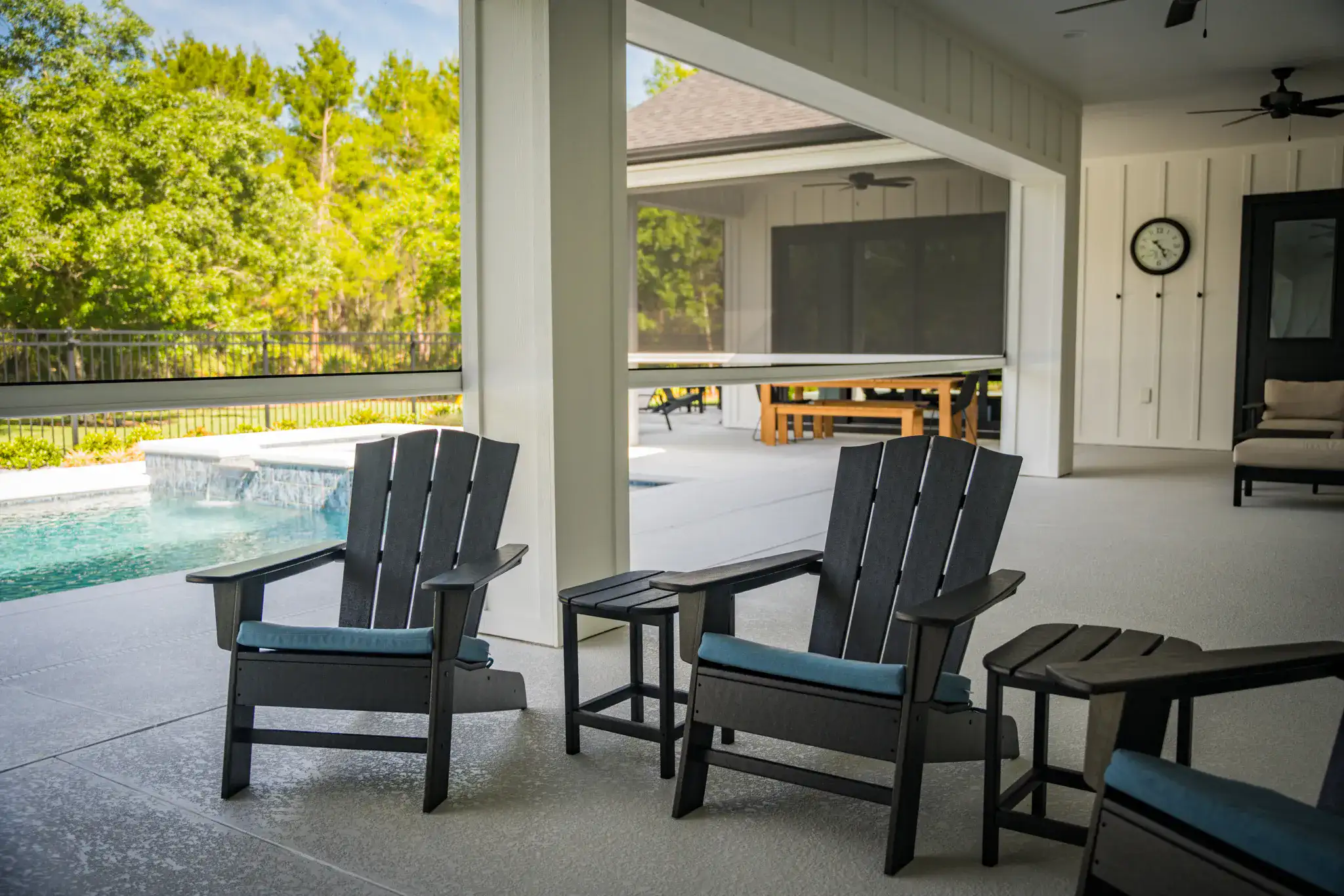 Adirondack chairs on a screened patio overlooking a pool under tree canopy