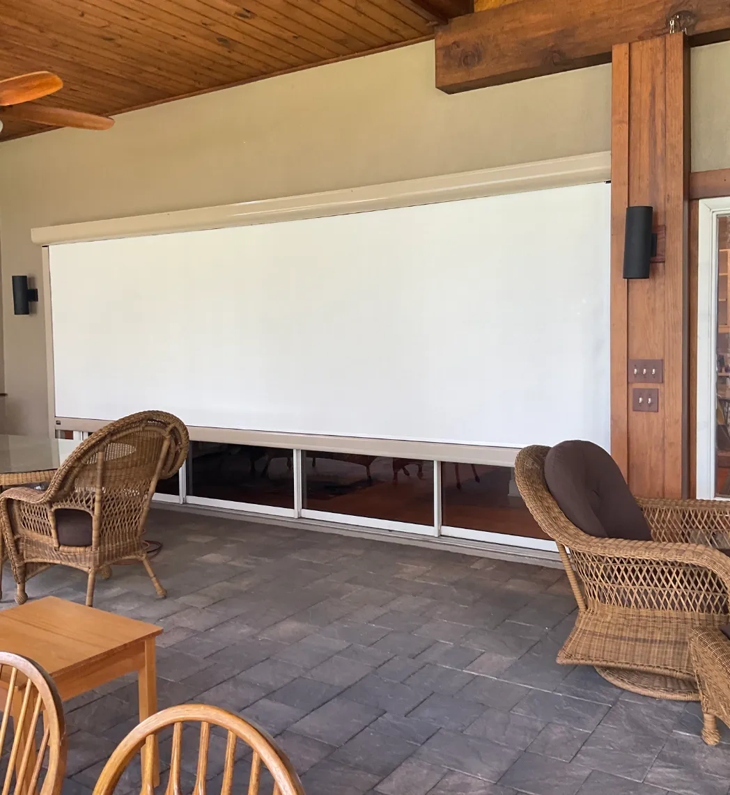 Solar screen fully lowered over sliding glass doors on a covered porch with wicker seating